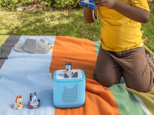 child playing with a blue toniebox 2 and three Bluey Tonies outside