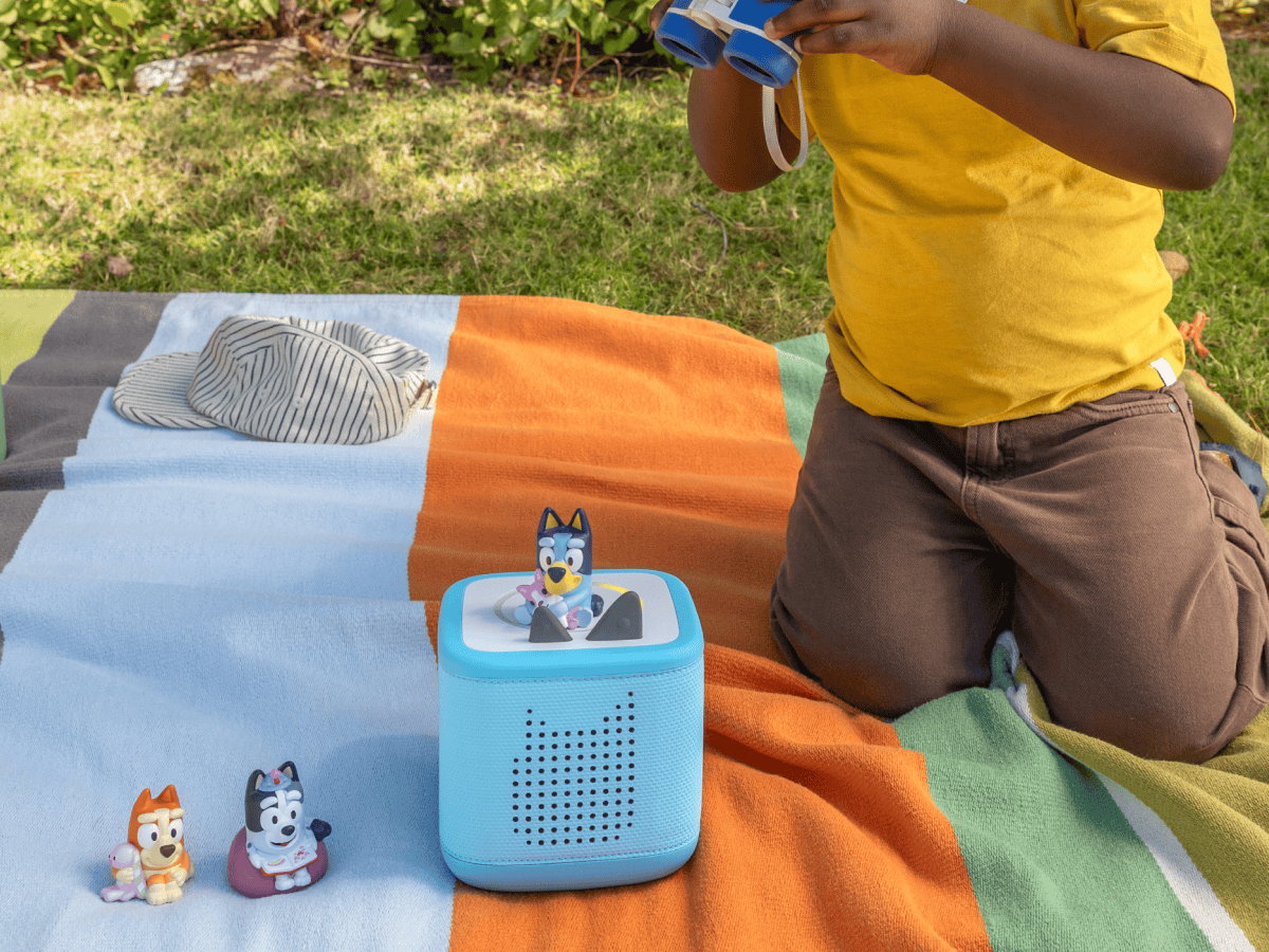 child playing with a blue toniebox 2 and three Bluey Tonies outside