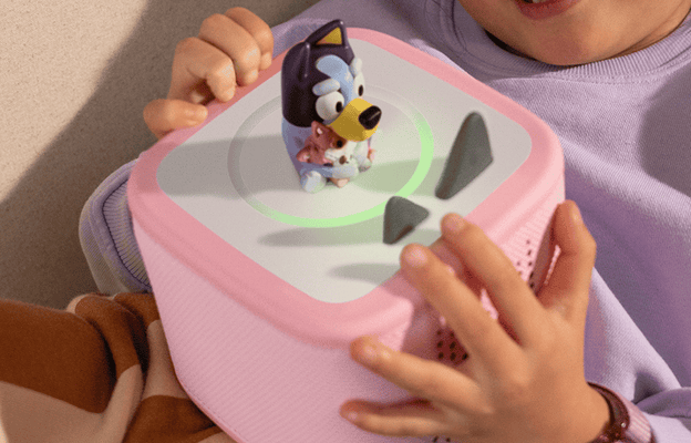 girl laying on the couch holding a pink Toniebox 2 with the Bluey Tonie on top