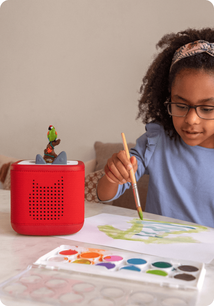 Child painting while listening to Nat Geo Kids Tonie on a red Toniebox 2