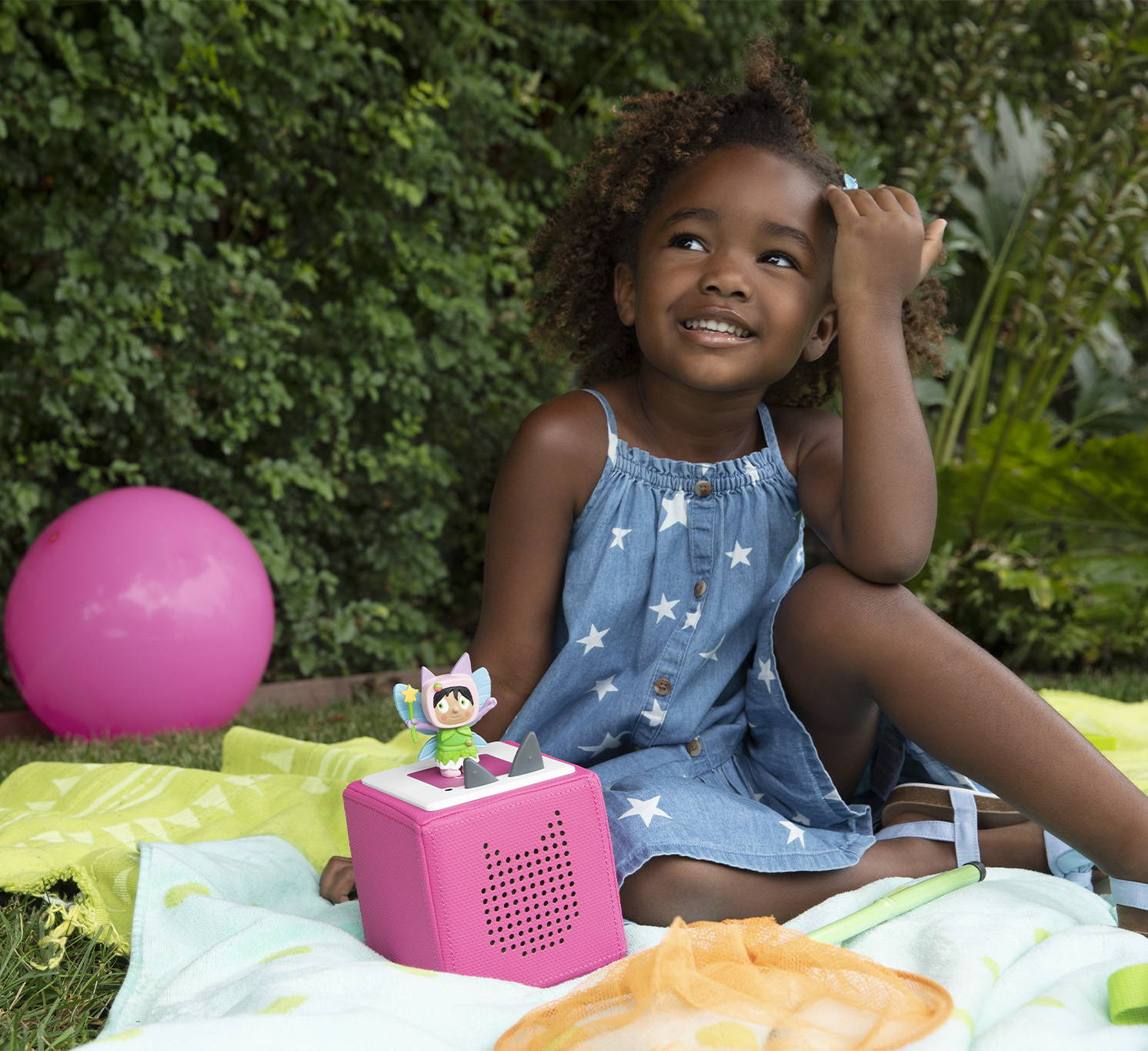 little girl sitting outside with a pink Toniebox and fairy Creative Tonie