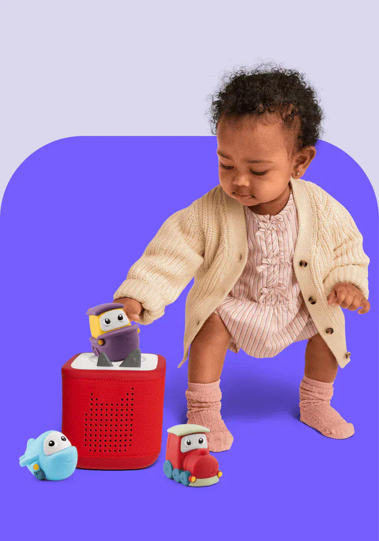 Child standing next to a red Toniebox 2 and the transportation set of My First Tonies